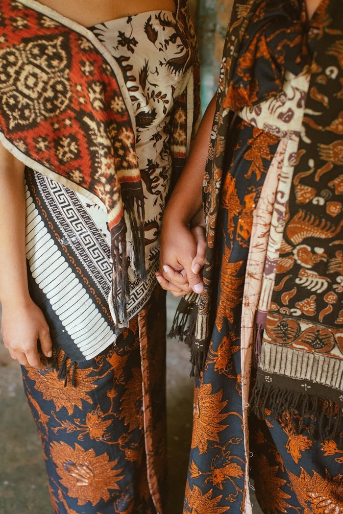 Close-up of two adults wearing traditional Balinese garments, holding hands indoors.