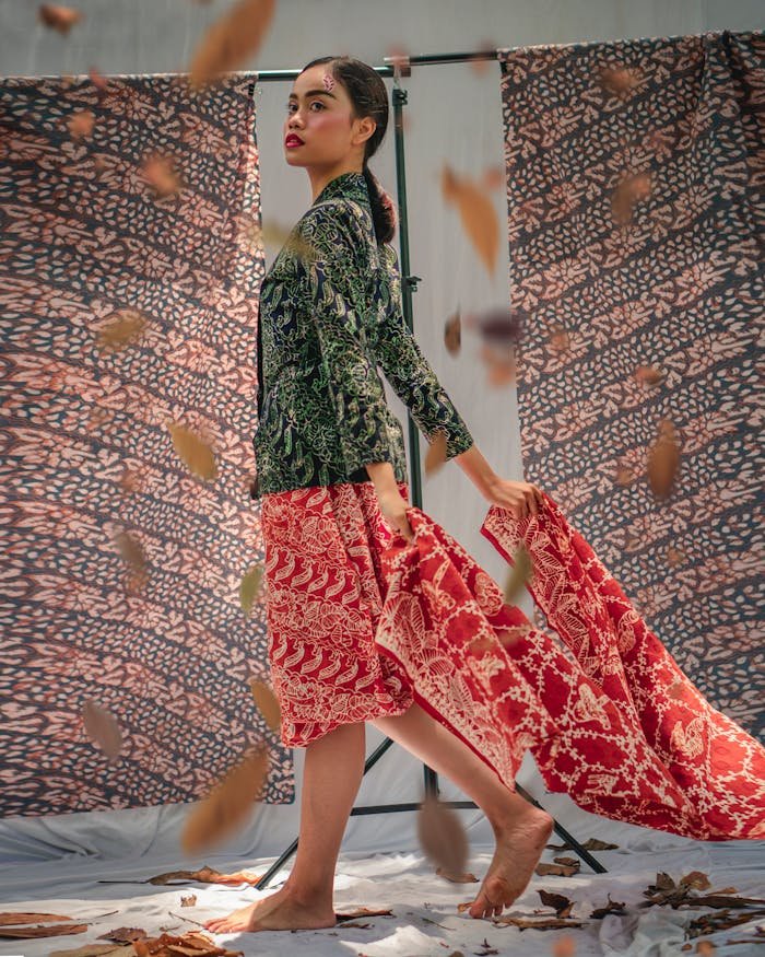 Portrait of a stylish woman in traditional Indonesian batik, with falling leaves and textile backdrop.